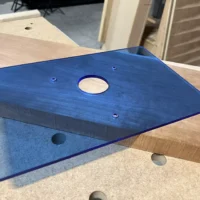Transparent blue acrylic base plate for Bosch 1617 plunge router, 12x8 inches, with center opening and mounting holes, displayed on wooden surface