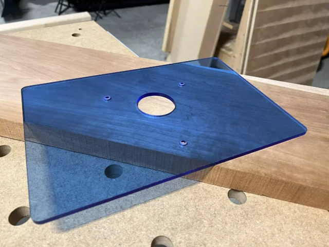 Transparent blue acrylic base plate for Bosch 1617 plunge router, 12x8 inches, with center opening and mounting holes, displayed on wooden surface