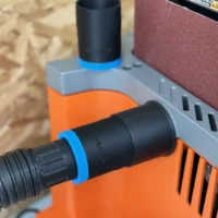 Black hose adapter with blue bands attached to Ridgid oscillating edge sander dust port, mounted on orange and gray sanding jig