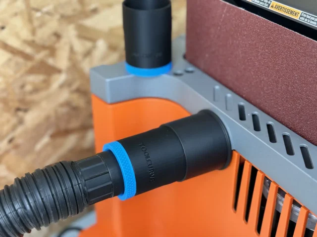 Black hose adapter with blue bands attached to Ridgid oscillating edge sander dust port, mounted on orange and gray sanding jig