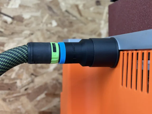 Black hose adapter with green and blue identification bands connected to a Ridgid oscillating edge sander with orange housing