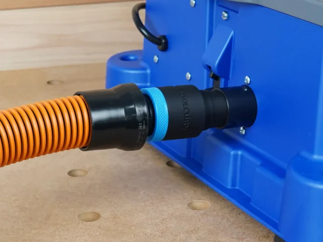 Black ToolCurve 1-1/4" hose adapter joining an orange hose to the rear dust port of a blue Kreg Foreman