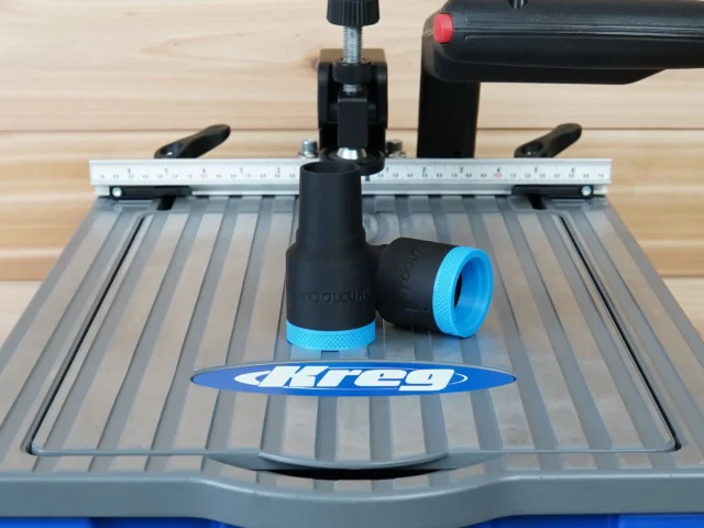 Black hose adapter with blue grip band attached to rear dust port of Kreg Foreman pocket-hole machine, shown on work surface