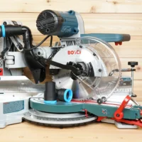 Black 36mm hose adapter with blue ring installed on a Bosch 10-inch glide miter saw dust port, second adapter on the table