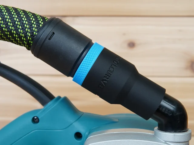 Black hose adapter with blue band attached to Makita belt sander dust port, connected to green and black braided hose