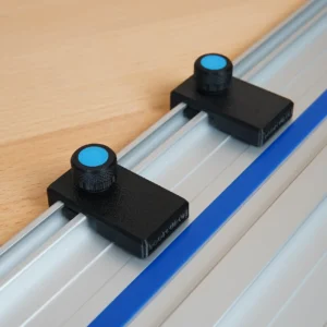 Two black limit stops with blue-capped knurled knobs mounted in the slot of a Kreg ACS guide rail