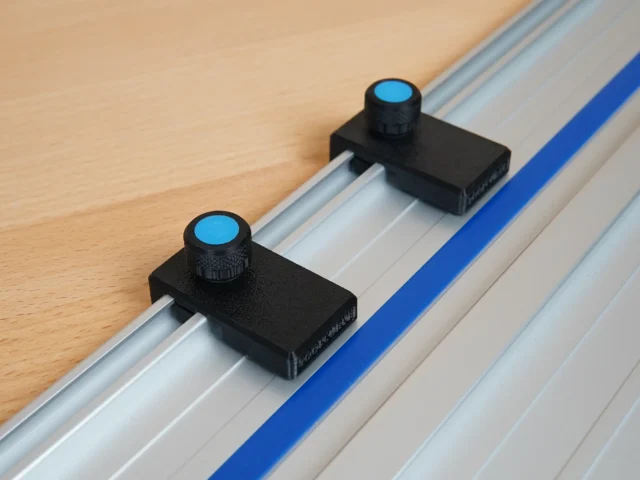 Two black limit stops with blue-capped knurled knobs mounted in the slot of a Kreg ACS guide rail