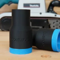 Two black hose adapters with blue textured grip bands, one upright and one tilted, shown on wood with a Makita belt sander blurred in background