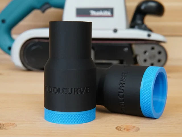 Two black hose adapters with blue textured grip bands, one upright and one tilted, shown on wood with a Makita belt sander blurred in background
