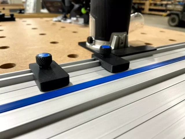 Two black limit stops with blue knurled knobs mounted on a Kreg ACS track saw guide rail, foreground and background positions