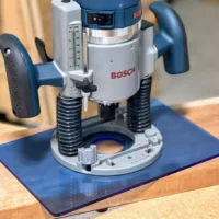 Blue transparent acrylic base plate mounted on a Bosch 1617 plunge router, showing 12 by 8 inch footprint on wooden surface