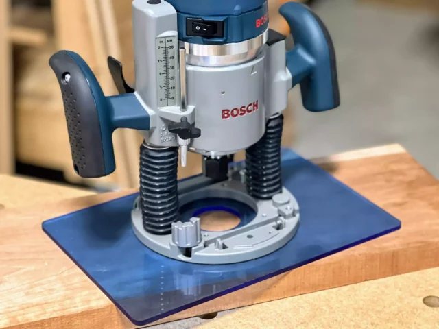 Blue transparent acrylic base plate mounted on a Bosch 1617 plunge router, showing 12 by 8 inch footprint on wooden surface