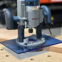 Blue transparent acrylic base plate attached under a Bosch 1617 plunge router on a wooden workbench with guide holes