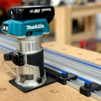 Kreg ACS limit stop mounted on a track saw guide rail next to a Makita router, showing the black cap and aluminum base with adjustment knob