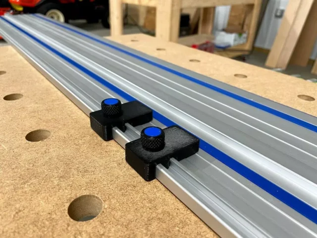 Two black limit stops with blue knurled knobs mounted on a Kreg ACS track saw guide rail