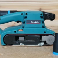 Black ToolCurve hose adapter with blue collar standing beside a Makita belt sander, adapter fitted to its dust port