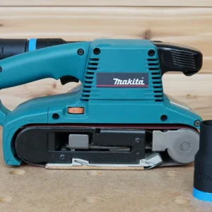 Black ToolCurve hose adapter with blue collar standing beside a Makita belt sander, adapter fitted to its dust port