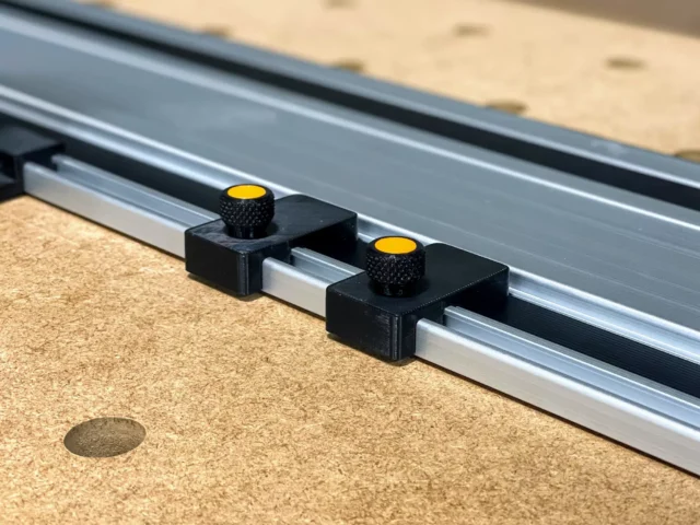 Two black limit stops with yellow knurled knobs mounted on a Powertec aluminum track rail, positioned on a workbench