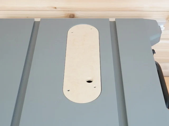 Cream-colored zero clearance insert seated in gray table saw top, showing central blade opening and mounting holes