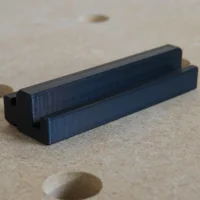 Black 3D-printed rail square holder with dual slots, designed to fit into an MFT/3 table t-track