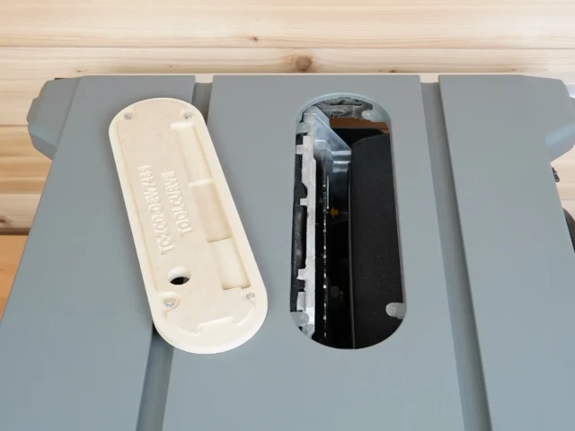 Cream-colored zero clearance insert and black interior insert side by side on gray Dewalt table saw top