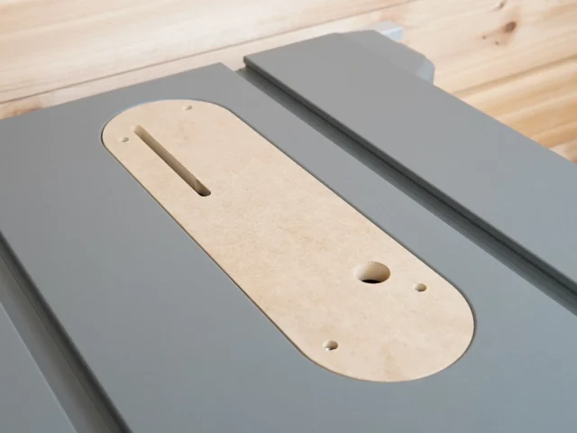 Natural wood zero clearance insert with slot and mounting holes, fitted in gray Dewalt table saw insert ring