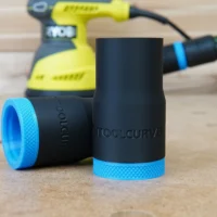 Black ToolCurve hose adapter with blue grip rings, shown disassembled in foreground with Ryobi sander blurred in background
