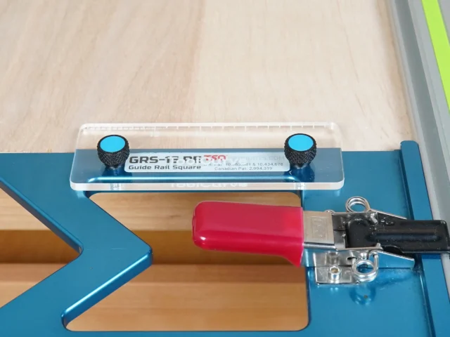 TSO guide rail square anti-tip support tab mounted on a blue track saw rail, showing two blue knobs and a red support block beneath the square