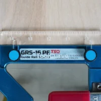 TSO Guide Rail Square Anti Tip Support Tab mounted on a blue guide rail square, showing the clear acrylic top with inch markings and two cyan support pegs