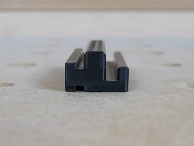 Black plastic rail square holder with dual slots, designed to mount on the side of an MFT/3 table t-track
