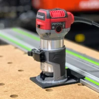 Avid Power compact router mounted on a guide rail adapter, positioned on a wooden workbench next to a green Festool track rail