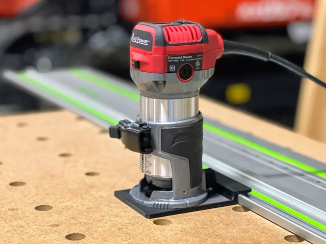 Avid Power compact router mounted on a guide rail adapter, positioned on a wooden workbench next to a green Festool track rail