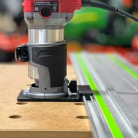 Avid Power compact router mounted on black ToolCurve adapter base, positioned on Festool-style guide rail over wooden workpiece