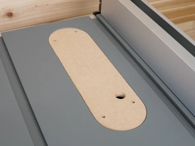 Beige MDF zero clearance insert for DeWalt table saw, positioned in the saw table with mounting holes and blade opening visible