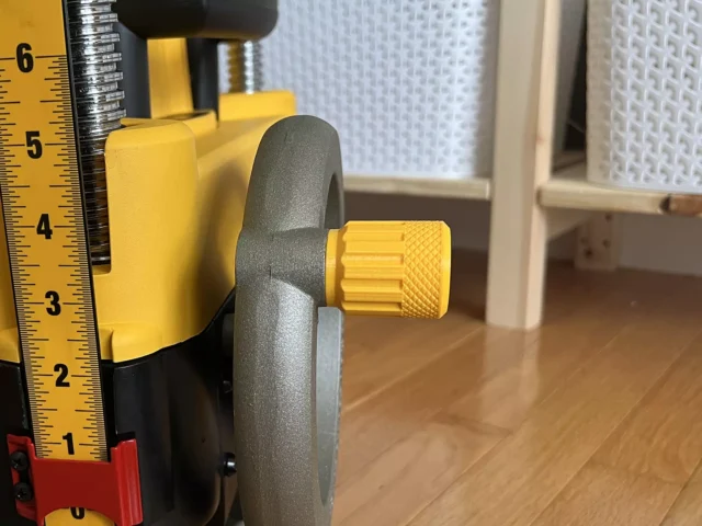 Yellow stubby handle with knurled grip attached to a DeWalt planer height adjustment crank, shown next to a ruler for scale