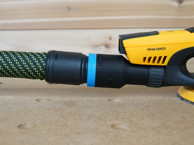 Hose adapter with blue band attached to Mirka Deros sander, connected to green braided hose