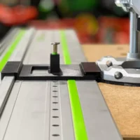 Black 3D-printed adapter with spring-loaded knob mounted on Festool LR32 rail with green strips, positioned over wooden workpiece