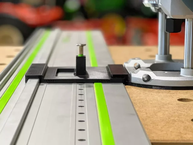 Black 3D-printed adapter with spring-loaded knob mounted on Festool LR32 rail with green strips, positioned over wooden workpiece