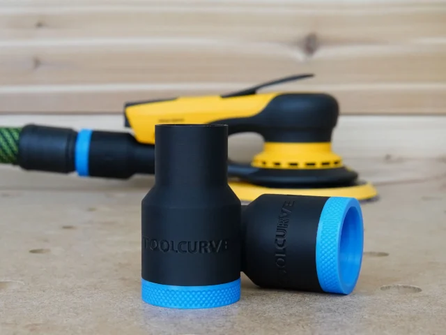Black ToolCurve hose adapter with blue grip ring, shown with Mirka sander and other tools on wood surface