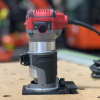 Red and gray Avid Power compact router mounted on a black base plate with guide rail adapter, viewed from front