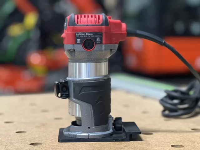 Red and gray Avid Power compact router mounted on a black base plate with guide rail adapter, viewed from front