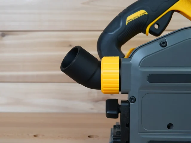 Yellow and black No Snag Dust Port adapter attached to a DeWalt track saw, with black hose angled upward from the adapter