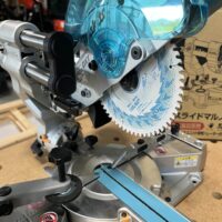 Makita LS610DZ 18v miter saw with blue dust collection hood and circular saw blade mounted on base, viewed from the side