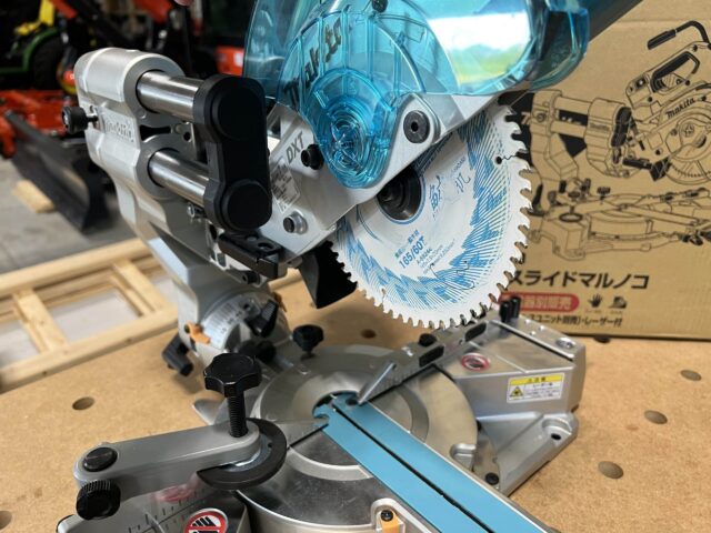 Makita LS610DZ 18v miter saw with blue dust collection hood and circular saw blade mounted on base, viewed from the side