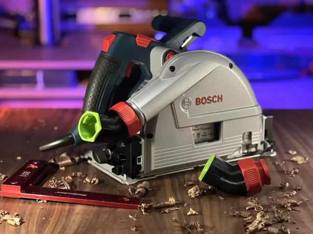 No Snag dust port adapter mounted on a Bosch track saw, showing the upward-angled hose connection with removable red collar