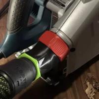 Red and green no-snag dust port adapter mounted on a Bosch track saw, with vacuum hose attached below