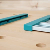 Two turquoise protective caps for Makita track saw rails, one showing the open channel end and one fitted onto a silver aluminum rail