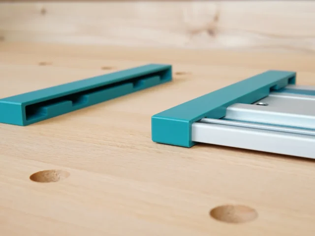 Two turquoise protective caps for Makita track saw rails, one showing the open channel end and one fitted onto a silver aluminum rail