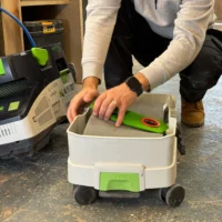 Bright green reusable filter bag with red handle inserted into white Festool MIDI dust extractor tank during use