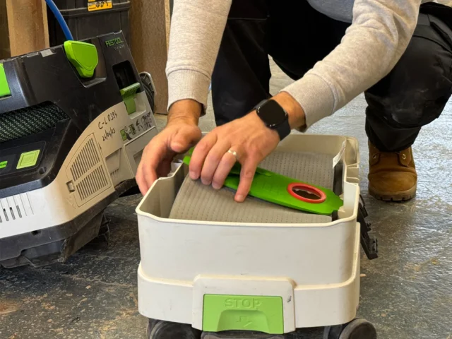 Bright green reusable filter bag with red handle inserted into white Festool MIDI dust extractor tank during use